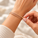 „Gönnen Sie sich eine kleine Berührung von Gold. Jeder Tag kann seinen eigenen Glanz haben.“  Manchmal genügt ein einziges Detail, damit ein ganzes Outfit neuen Charme erhält. Das goldene magnetische Armband Variace aus der Kollektion Kraft der Farben besticht durch seinen warmen Farbton, die feine Struktur der Kordel und die Möglichkeit, sein Aussehen je nach Stimmung zu verändern. Wickeln Sie es um Ihr Handgelenk und lassen Sie die einzelnen Reihen ordentlich nebeneinander liegen, kreuzen Sie sie leicht oder schaffen Sie eine lockerere Anordnung. Ein Schmuckstück gibt Ihnen Raum für Ihre eigenen Variationen. Allein wirkt es zart und elegant. In Kombination mit Mineralarmbändern verleiht es Ihrem Ensemble einen hellen, festlicheren Akzent. Es kommt neben Weiß, Creme, Braun und Schwarz wunderschön zur Geltung.  Der Zauber liegt in der Kordel selbst  Es geht nicht nur um den Magnetverschluss. Die magnetischen Teile der Kordel haften beim Umwickeln aneinander, sodass Sie keinen kleinen Karabiner schließen oder nach einer Öse suchen müssen. Sie wickeln die Kordel einfach um Ihr Handgelenk, legen ihre Teile aneinander und stimmen die Position der Enden ab. Größe und Anordnung der Reihen können Sie in dem Rahmen anpassen, den die Gesamtlänge von 51 cm erlaubt. Die Anzahl der Wicklungen hängt vom Umfang Ihres Handgelenks ab.  Gold – die Farbe des Lichts und besonderer Augenblicke  Der goldene Farbton erinnert an Sonnenlicht, Wärme und Momente, die es wert sind, bewahrt zu werden. In der Kollektion Kraft der Farben können Sie ihn als persönliches Symbol für Freude, Fülle und das Bewusstsein des eigenen Wertes annehmen. Tragen Sie ihn als kleine Erinnerung daran, dass Sie sich auch an einem gewöhnlichen Tag etwas Schönes gönnen dürfen. Oder schenken Sie ihn einem Menschen, dem Sie sagen möchten: „Du bist mir kostbar.“  Ein Schmuckstück, mehrere Möglichkeiten  Am Handgelenk gestalten Sie ein mehrreihiges Armband ganz nach Ihrem Geschmack. Die Länge der Kordel bietet auch die Möglichkeit, sie als kurze Halskette auszuprobieren — sofern der Halsumfang ein angenehmes Tragen und eine ausreichende Überlappung der magnetischen Teile erlaubt. Verändern Sie sein Aussehen je nach Kleidung und Anlass. Einmal ein dezentes Accessoire, das andere Mal ein markanterer Bestandteil Ihrer Lieblingskombination.  Warum Sie es lieben werden Variables Aussehen: Die einzelnen Reihen ordnen Sie ganz nach Ihren Vorstellungen an. Einfaches Anlegen: ohne klassischen Verschluss und kleine Ösen. Anpassbarer Umfang: durch Umwickeln und Überlappen der Kordel. Feine Ausführung: Die etwa 2 mm starke Kordel kommt auch in mehreren Reihen schön zur Geltung. Warmer goldener Farbton: für alltägliche Eleganz und festlichere Momente. Leicht kombinierbar: mit Uhren, Mineralarmbändern und weiteren Accessoires. Für wen es geeignet ist  Für Liebhaber warmer Farbtöne, zarten Schmucks und Accessoires, die sich dem eigenen Stil anpassen lassen. Es eignet sich für Frauen und Männer, die gerne goldene Töne tragen.  Es erfreut auch als Geschenk — der Beschenkte entscheidet selbst, wie er es tragen und welche persönliche Bedeutung er ihm geben möchte.  So legen Sie das Armband an Wickeln Sie die Kordel so um Ihr Handgelenk, dass sie bequem sitzt. Legen Sie die magnetischen Teile aneinander und lassen Sie sie haften. Richten Sie die einzelnen Reihen und die Position der Enden aus. Prüfen Sie vor dem Tragen, dass die Überlappung gut hält.  Beim Abnehmen die Teile vorsichtig voneinander lösen, ohne ruckartig an den Endstücken zu ziehen.  Material und Maße Farbe der Kordel: goldener Farbton. Gesamtlänge: 51 cm. Stärke der Kordel: ca. 2 mm. Ausführung: magnetische Kordel mit textilem Oberflächenfinish. Endstücke: Metall, in goldener Farbe. Größe beim Tragen: anpassbar je nach Wicklung und Überlappung. Lieferumfang: 1 Stück.  Die Bezeichnung „golden“ beschreibt die Farbgestaltung, nicht die Herstellung aus Edelmetall.  Pflege des Armbands  Legen Sie es als Letztes an und nehmen Sie es als Erstes ab. Schützen Sie die Kordel und die Endstücke vor Parfüm, Kosmetik, Reinigungsmitteln und langem Einweichen. Legen Sie das Armband vor dem Baden, Sport und Schlafen ab. Reinigen Sie es mit einem weichen trockenen oder leicht angefeuchteten Tuch und lassen Sie es frei an der Luft trocknen, außerhalb direkter Sonneneinstrahlung. Trennen Sie die magnetischen Teile schonend voneinander.  Der Magnetismus dient dem Haften und der Anordnung der Kordel. Das Armband ist ein Modeaccessoire, kein Heilmittel.  Kraft der Farben – Ihr Stil, Ihre Variationen.